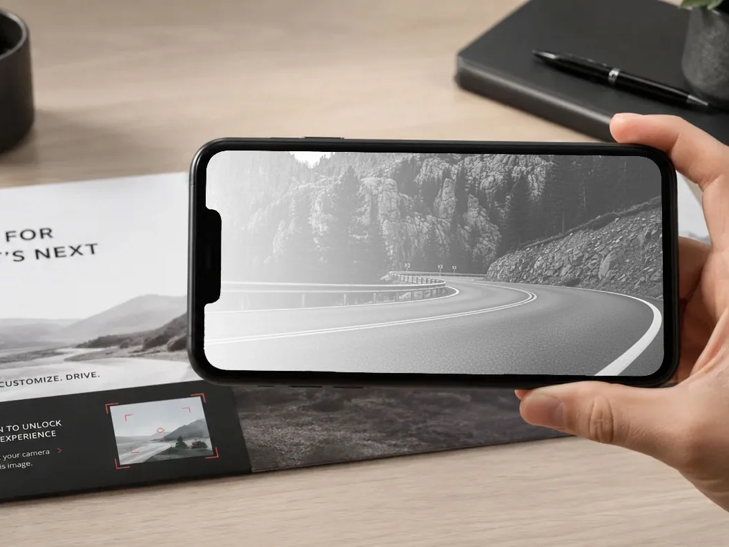 A hand holding a phone over a printed brochure on a desk.